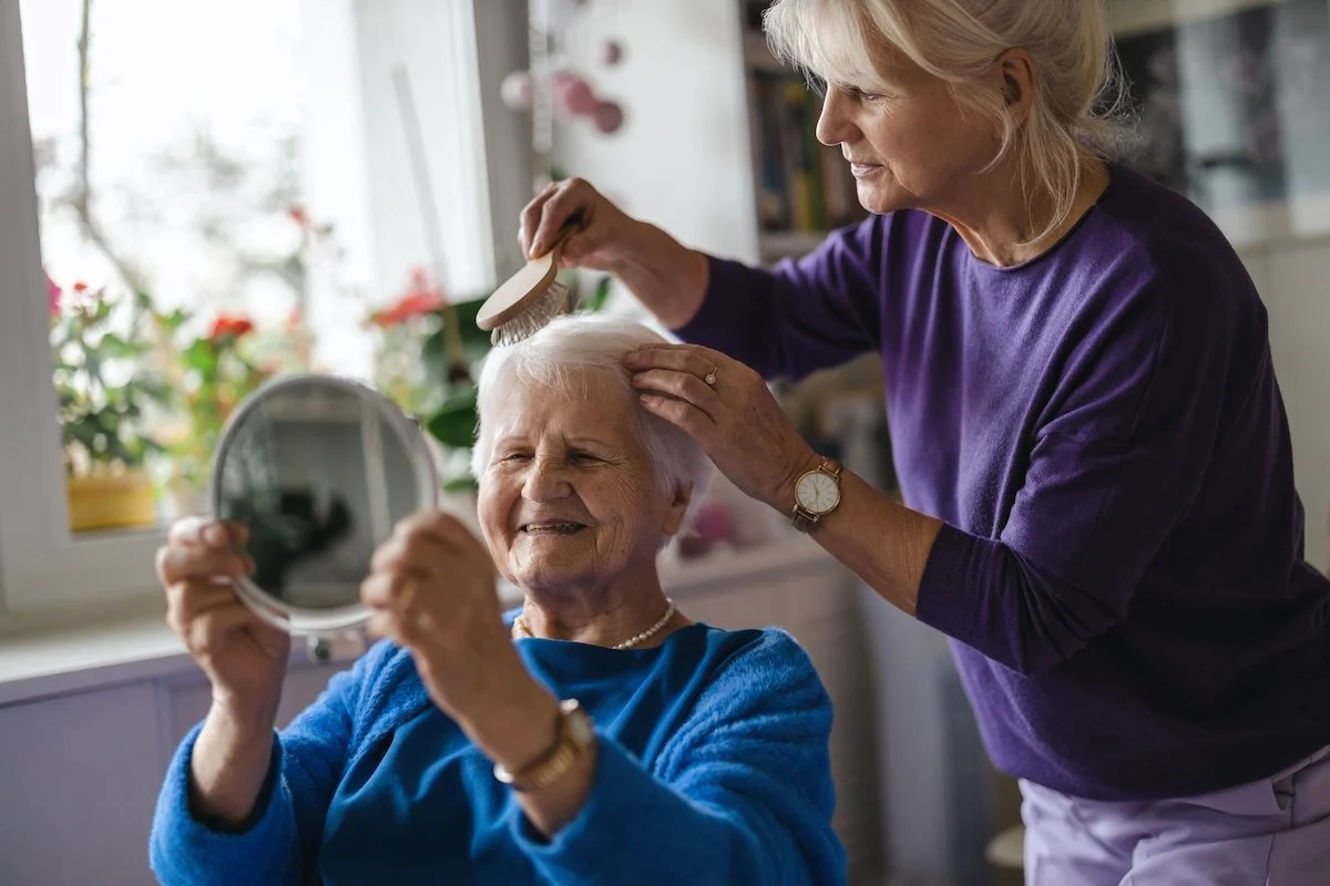 Pflegerin kämmt liebevoll die Haare einer älteren Frau – Haushaltshilfe und Betreuung