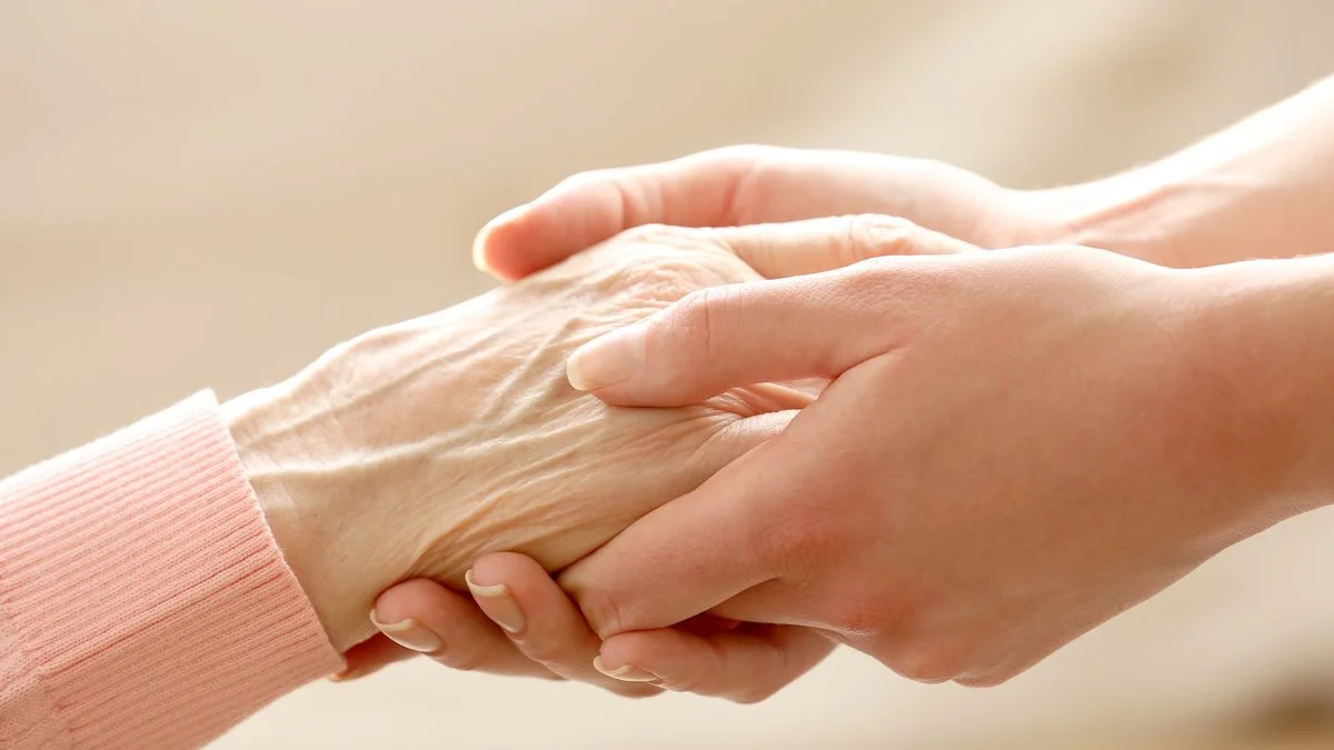 Pflegerin hält liebevoll die Hände einer älteren Person – Palliativpflege zu Hause