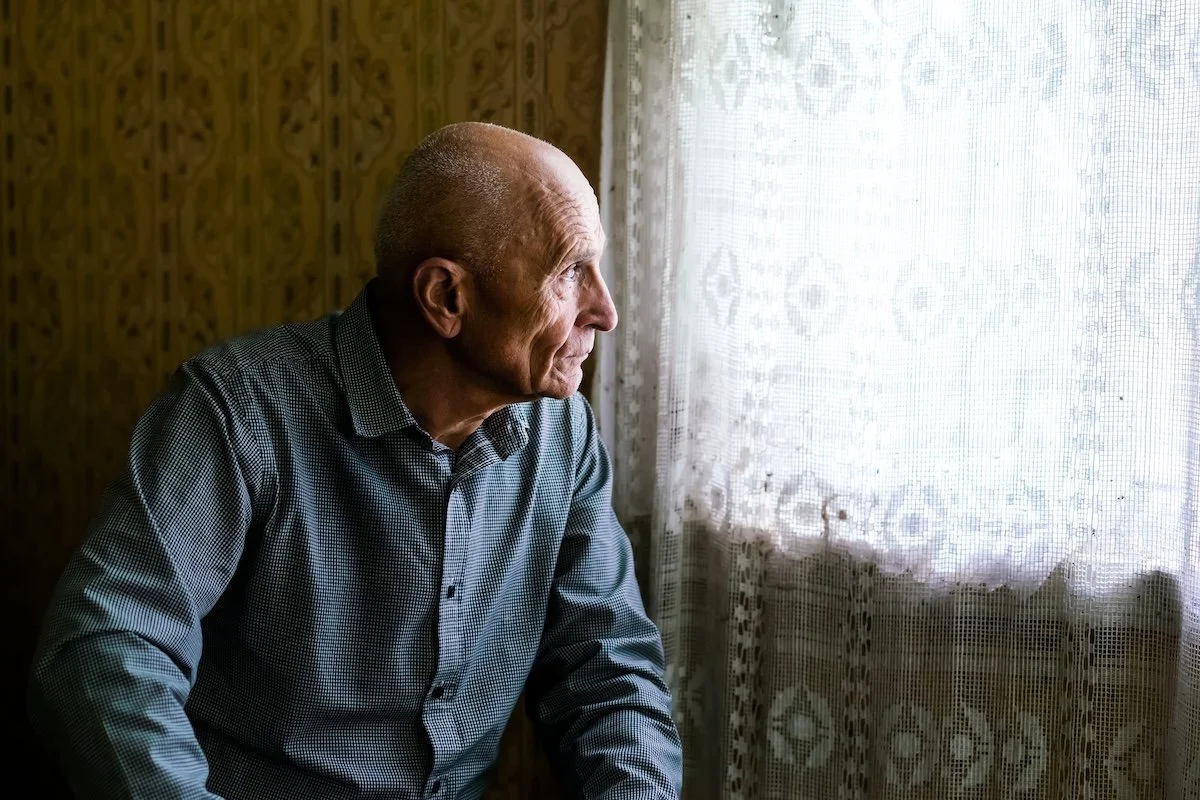 Älterer Mann schaut nachdenklich aus dem Fenster – Demenzpflege und Begleitung zu Hause